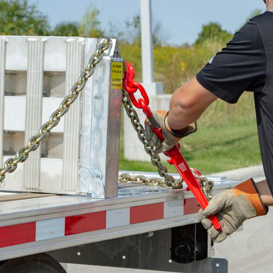 HD Ramps loading ramps stored in ramp brackets on a step deck trailer with a large-wheeled vehicle